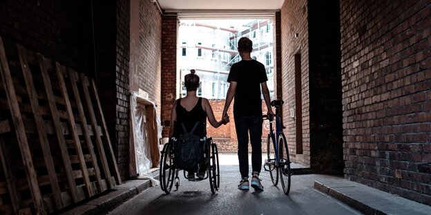 Ein Radfahrer und eine Rollstuhlfahrerin gehen gemeinsam durch einen Hauseingang