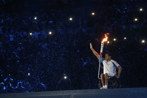 Im Rolllstuhl sitzender Schwimmer Silva Clodoaldo entzündet olympisches Feuer auf der Bühne bei der Eröffnungsfeier