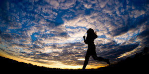 Eine Frau joggt im Sonnenuntergang über ein Feld, zu sehen ist nur ihre Silhouette