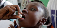 Eine Person füllt einem Mädchen mit einem kleinen Fläschchen ein Cholera-Impfmittel in den Mund