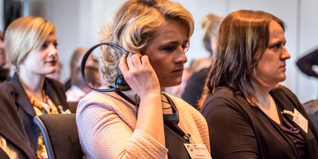 Eine Frau hält sich bei einer Veranstaltung ein Headset ans Ohr.