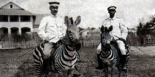 Zwei weiße Männer sitzen auf Zebras