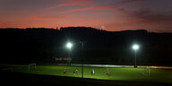 Ein Fußballplatz im Flutlicht, es dämmert, der Himmel ist rosa, die Umgebung schwarz