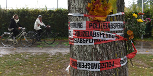 Um einen Baum ist Absperrband der Polizei gewunden, in das Blumen und Blätter gesteckt wurden