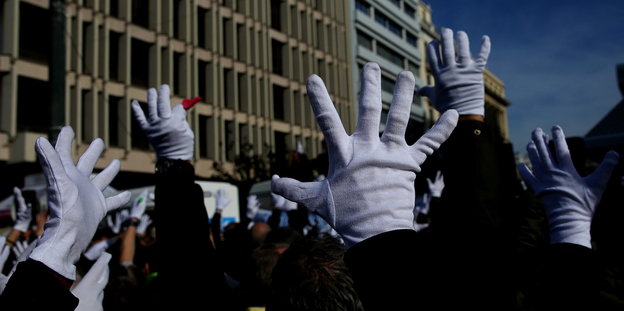 Hände in weißen Handschuhen und gespreizten Fingern sind in die Höhe gestreckt