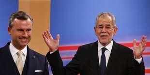 Alexander Van der Bellen (r.) hebt die Arme, daneben steht Norbert Hofer (l.) und lächelt künstlich