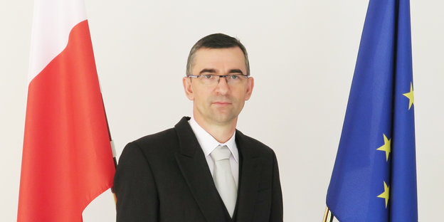 Ein Mann mit Brille steht zwischen einer EU- und einer polnischen Flagge