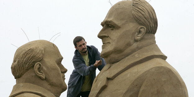 Ein Mann klettert auf zwei übergroße Sandfiguren
