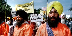 Sikhs in orangefarbener Kleidung und Turbanen halten Säbel vor sich