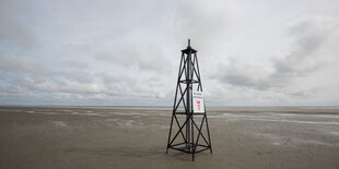 Ein gefakter Bohnturm steht am Strand, dahinter das Meer