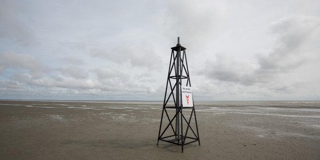Ein gefakter Bohnturm steht am Strand, dahinter das Meer
