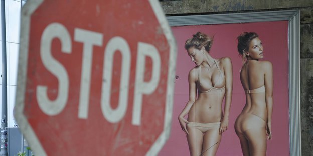 Im Hintergrund eine Frau im Bikini auf einem Werbeplakat. Davor ein Stop-Schild