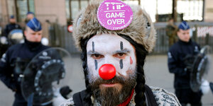 Ein TTIP-Demonstrant mit roter Clownsnase und Fellmütze, dahinter Polizisten