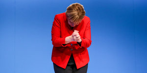 Angela Merkel schaut nach unten, ihre Hände sind gefaltet