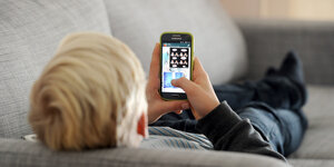 Ein kleiner Junge liegt auf einem Sofa und spielt mit einem Iphone