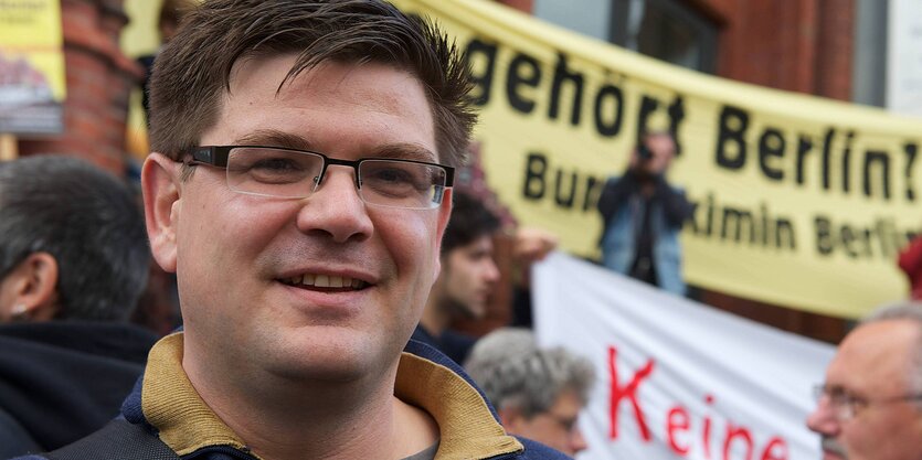 Porträt Andrej Holm vor Demonstranten mit Transparent