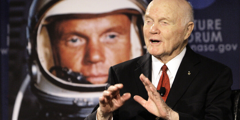 US-Astronaut John Glenn gestikuliert vor einem Plakat von sich selbst