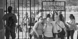 Drei Touristen posieren vor dem KZ-Tor mit der Inschrift „Arbeit macht frei“