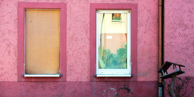 Zwei Fenster und eine rosa Hauswand, eines davon mit Holz statt Glas