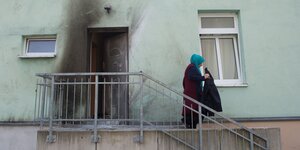 Eine Frau steht vor der verrußten Tür eines Gebäudes