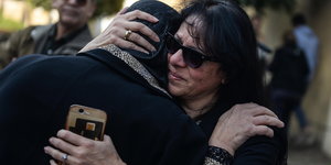 Zwei Frauen, beide schwarz gekleidet, umarmen sich weinend