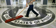 ein Mann wischt den Boden, darauf ist ein großes CIA-Logo
