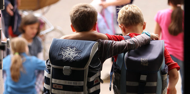 Zwei Kinder umarmen sich mit Schulranzen auf dem Rücken