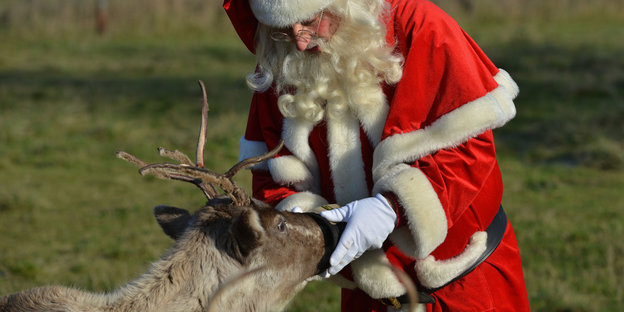 Der Weihnachtsmann streichelt ein Rentier