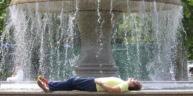 Ein Mann liegt auf dem Rücken ausgestreckt am Rande eines Springbrunnens
