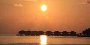 Die Sonne hängt tief und gelb über dem Wasser, das ein Ferienressort auf den Malediven umgibt