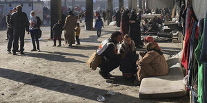 Freistehende Betonpfeiler und viele Menschen, die teils auf Matratzen sitzen in der Massenunterkuft in Jibreen