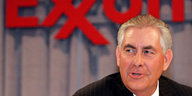 Rex Tillerson sitzt im Anzug vor dem Exxon-Logo