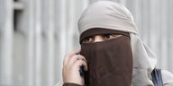 Eine Frau trägt den Nikab, ein Tuch, das den Kopf bis auf die Augenpartie verhüllt.