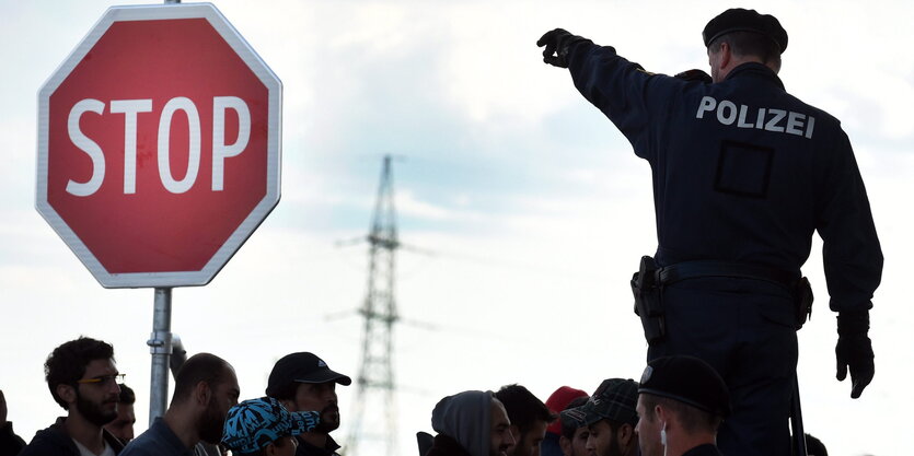 Ein Polizist steht mit ausgestrecktem Arm über einer Gruppe Flüchtender, neben ihm ein Stoppschild