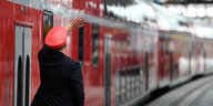 Ein Bahnmitarbeiter steht neben einem roten Zug und winkt mit der linken Hand