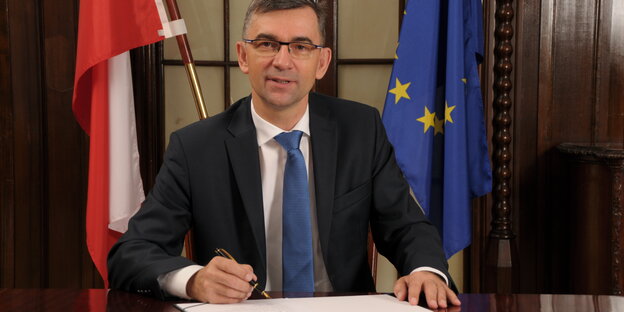 Der polnische Botschafter sitzt vor einer polnischen und einer EU-Flagge