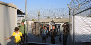 Jugendliche stehen hinter einem Zaun mit Stacheldraht