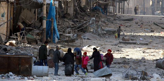Eine Gruppe Männer, Frauen und Kinder steht in den Trümmern Aleppos beisammen