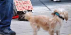 Ein Bettler mit einem Schild auf dem steht: Ich habe Hunger. Davor ein Hund