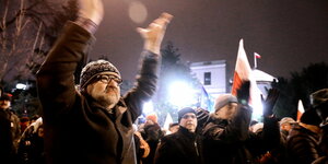 Ein Mann steht in einer Gruppe von protestierenden Menschen vor dem polnischen Parlament und klatscht über sienem Kopf die Hände zusammen