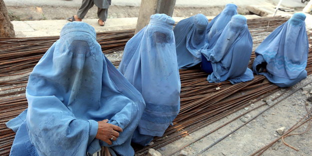 Sechs Frauen in hellblauen Burkas sitzen auf einem Stapel aus Metallstangen