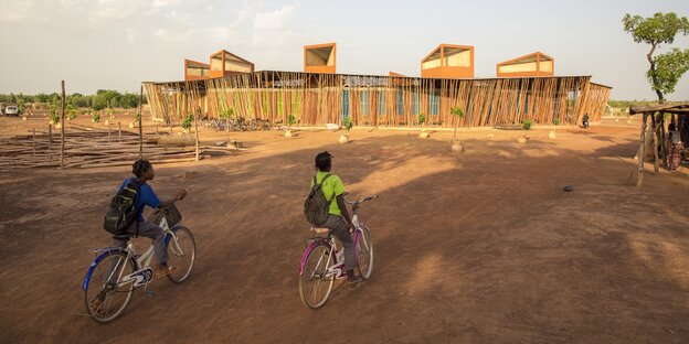Zwei Kinder auf dem Fahrrad fahren auf einen Schulbau zu