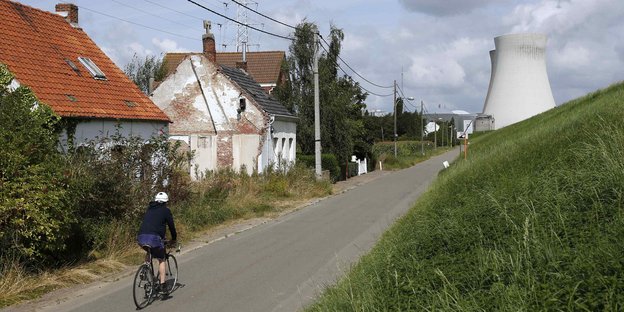 Ein Radler fährt durch ein Dorf. Hinten am Horizont steht der Kühlturm eines Atomreaktors