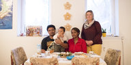 Vater, Mutter und Kind sitzen an einem Tisch mit Christstollen und Kerzen, daneben steht eine Frau
