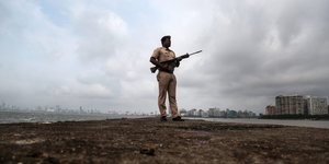 Ein indischer Polizist steht mit seiner Waffe vor der Skyline Mumbais