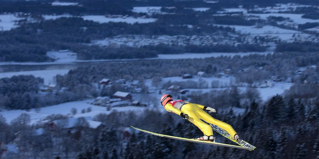ein Mann mit Skiern in der Luft, im Hintergrund eine verschneite Landschaft
