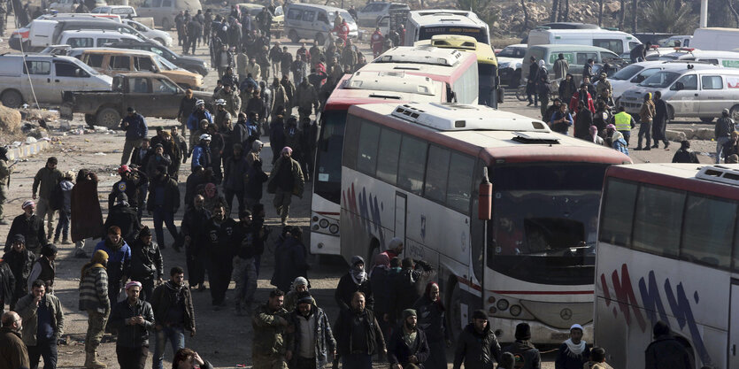 Mehrere Busse und Autos stehen auf einem Platz, viele Menschen steigen ein oder aus