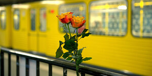 Blumen stecken an einem Geländer, im Hintergrund eine gelbe U-Bahn