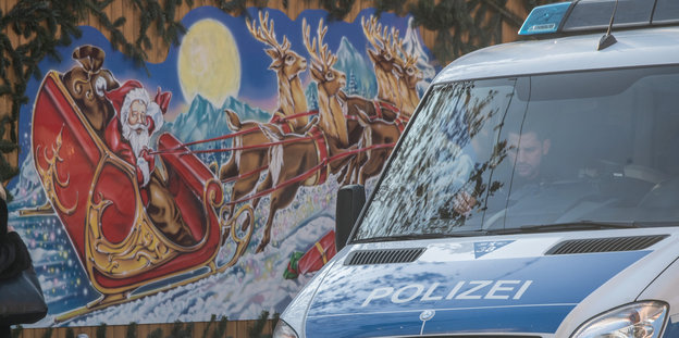 Ein Polizeiauto steht vor einer Weihnachtsmarktbude mit buntem Weihnachtsmann-Motiv