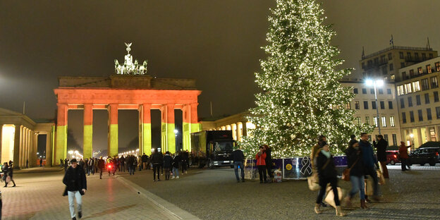 das Brandenburger Tor in schwarz-rot-gold, davor ein Weihnachtsbaum